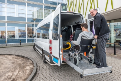 Une personne à mobilité réduite et un accompagnateur montent dans un véhicule adapté